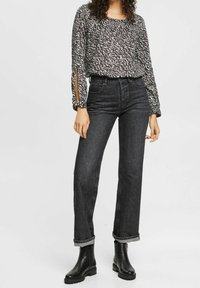 Blusa nera a maniche lunghe con motivi, dotata di fessure laterali, abbinata a jeans scuri a vita alta e stivaletti neri.