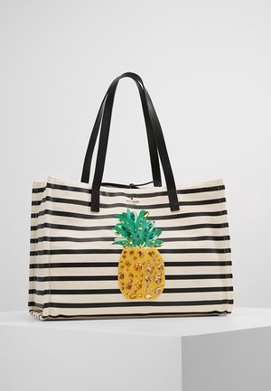 Canvas-tote taske med sort-hvide vandrette striber, sorte håndtag og en dekoreret gul og grøn ananas på forsiden.