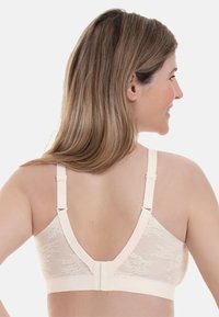 Lys beige blonded lace bh med brede stropper og lav rygg. Har justerbare stropper og krok-lukking for sikker passform. Glatt tekstur.
