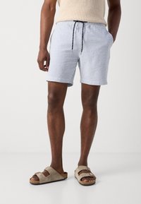 Men's light blue patterned shorts made of textured fabric, featuring an elastic waistband with drawstring and side pockets, paired with beige sandals.