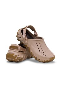 Lichtbeige klompen met een gestructureerde buitenzool, verstelbare riem en ventilatiegaten, met een robuust ontwerp en een zachte binnenvoering.