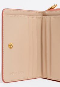 Interior de la cartera Bimba y Lola en suave cuero beige, con compartimentos para tarjetas, un botón de presión dorado y textura suave, con un acento coral en el borde.