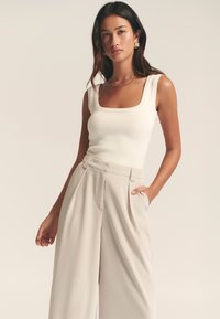 Cremefarvet ribbet tanktop med firkantet udskæring, kombineret med højtaljede beige bukser med brede ben. Glat stof med skrå lommer.