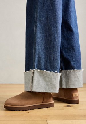 Bocanci din suede maro, cu talpă din cauciuc plat, asortați cu blugi dark denim cu croială largă, având manșete din denim deschis, ciufulite.