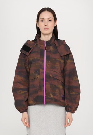 Bruine camouflagejack met capuchon, oversized pasvorm en elastische manchetten. Voorzien van een paarse rits en schoudertabs voor extra detail.