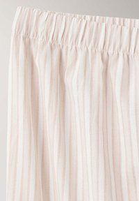 Tissu de couleur claire avec de fines rayures rouges verticales et une ceinture élastique, probablement partie d'un vêtement.