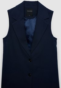 Marineblauer ärmelloser Blazer mit Reverskragen, zwei Vorderentaschen und schwarzen Knöpfen; das Innere ist mit einem glatten blauen Futter versehen. Markenetikett sichtbar.