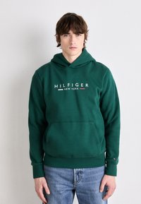 Zelena pamučna dukserica s prednjim džepom, podesivom kapuljačom i "HILFIGER NEW YORK" logom u bijeloj, crvenoj i zelenoj boji.