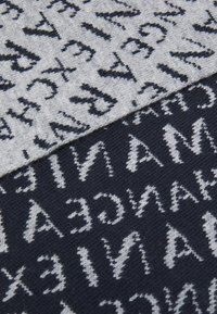 Pletená tkanina s striedajúcimi sa šedými a tmavomodrými časťami. Dizajn obsahuje veľké, kontrastné textové vzory v bielej farbe, ktoré vytvárajú výrazné vizuály.