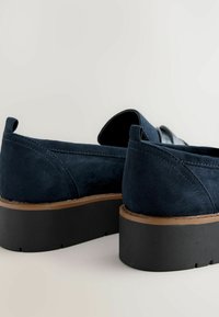 Navy blue suede shoes with a rounded toe, flat black platform sole, and brown accent along the edge, featuring simple stitching detail.