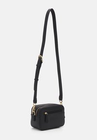Sac bandoulière noir en cuir lisse. Présente des accessoires en métal doré, des compartiments à double fermeture éclair et une bandoulière réglable. Forme rectangulaire compacte.