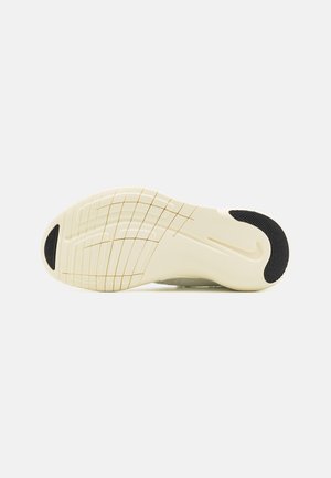 Semelle d'une sneaker couleur crème avec des patins antidérapants noirs au talon et à l'orteil, présentant des rainures courbes et un logo discret de la marque près de la voûte plantaire.