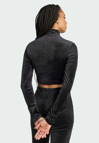 Svart avkortad långärmad topp gjord av ett mjukt, sammetsliknande material med hög krage, stylad med slim-fit svarta byxor.