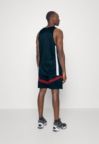Sort atletisk tanktop med hvide sidepaneler, parret med sorte shorts med røde skråstriber. Mat stof med en afslappet pasform.