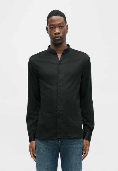 Mustapaita, jossa on pitkät hihat ja nappikaulus, hienovarainen rakenne ja kapea malli. Yhdistetty sinisiin farkkuihin.