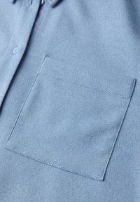 Helles blaues Hemd mit Knöpfen aus strukturiertem Stoff, ausgestattet mit einer Brusttasche und einem spitzen Kragen. Glatte Oberfläche und saubere Nähte.