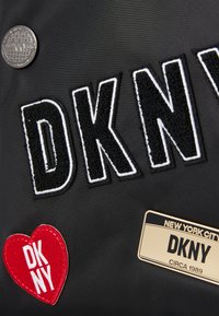 Black fabric with "DKNY" in large black embroidered letters outlined in white. Includes a red heart patch with white text and a gold nameplate.