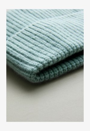 Minkštas, dryžuotas megztinis šviesiai mėlynai žaliame audinyje, sulankstytas, kad būtų matoma tekstūra ir gylis, su švariu krašto apdailu.