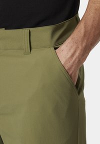 Pantalones de tela verde con una textura suave, que presentan un bolsillo lateral y una cinturilla plana. Las costuras visibles se alinean con el diseño contemporáneo.