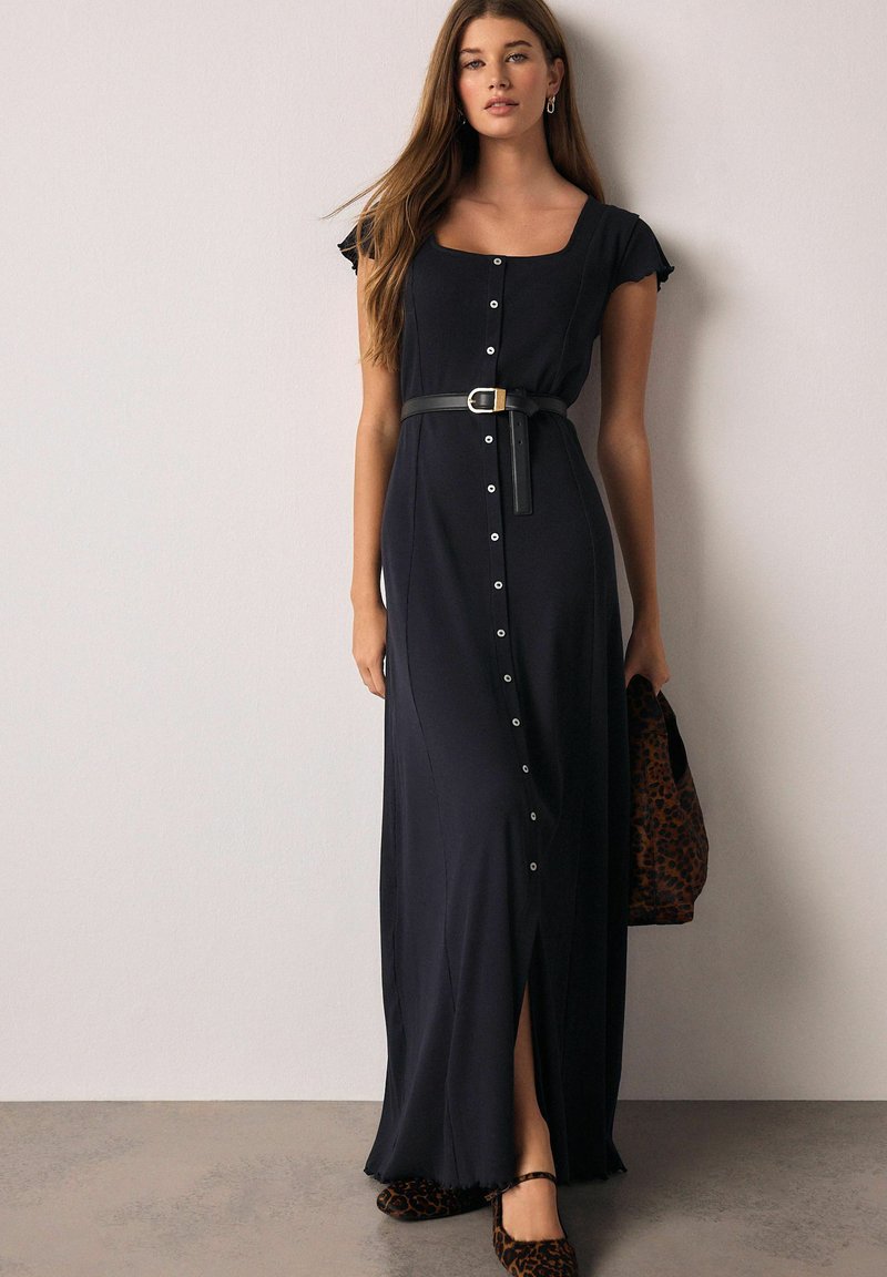 Tengerészkék maxiruha négyzet alakú nyakkivágással, rövid fodros ujjak, gombos elülső rész, combközépig érő hasítékkal, fekete övvel és állatmintás táskával párosítva.