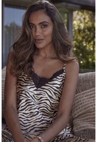 Satin top met een zwart-witte zebraprint en kant langs de halslijn, gecombineerd met textuurachtige beige kussens op de achtergrond.