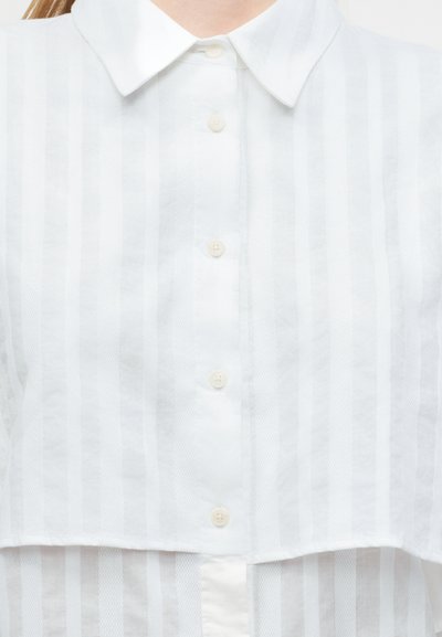 Άσπρο πουκάμισο με γιακά και κάθετες διαφανείς ρίγες, με τέσσερα ορατά κουμπιά στο μπροστινό μέρος, φορεμένο από ένα άτομο που κόβεται στο ύψος του λαιμού.