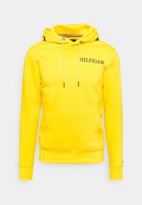 Felpa con cappuccio gialla in cotone, dotata di tasca frontale, cappuccio con coulisse e logo "HILFIGER" in nero. Tessuto liscio e polsini a costine.