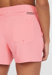 Rosa simbyxor med en bakficka med knapp, märkt "O'Neill Hyperdry," med slät tyg och förstärkta sömmar.