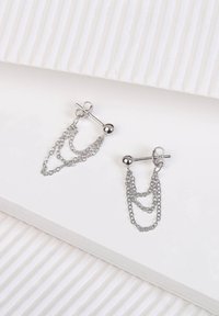 Zilveren oorbellen met laagjes kettingen en een sferische stud. De oorbellen hebben een slanke, metalen afwerking en minimale textuur.