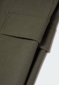 Tissu vert olive à la texture lisse, présentant un pliage et une poche plaquée rectangulaire intégrée au matériau.