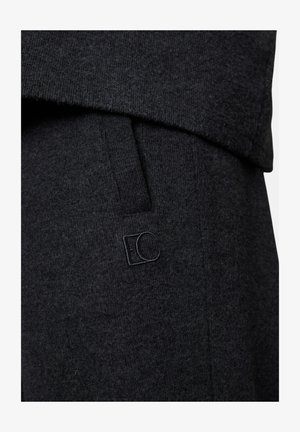 Close-up of dark gray knitted fabric with a pocket and subtle embroidered "EC" logo on the clothing.