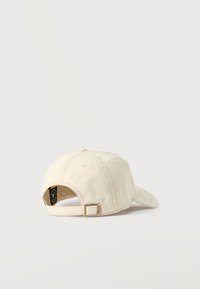 Béžová nastavitelná baseballová kšiltovka s kovovou přezkou a našitými větracími otvory, zobrazena zezadu na bílém pozadí.