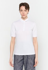 White short-sleeve polo shirt with a buttoned placket, made from a smooth, lightweight fabric. Features a subtle logo detail on the chest.