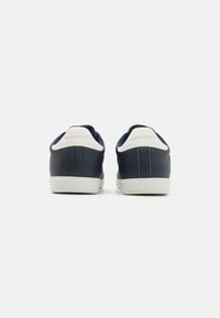 Navy blue sneakers with a smooth leather upper, white soles, and contrasting white heel accents. Minimalist design with a rounded shape.