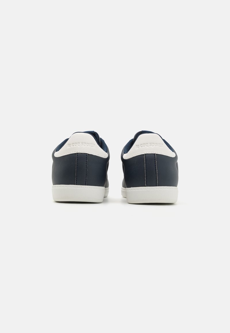 Zapatillas de deporte azul marino con parte superior de cuero suave, suelas blancas y acentos en el talón en blanco. Diseño minimalista con forma redondeada.