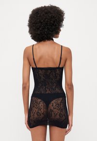 Vestido preto de renda com alças ajustáveis, corpete justo e costas transparentes, apresentando padrões florais e uma bainha godê.