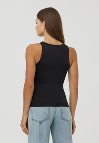 Czarny top na ramiączkach o dopasowanym kroju i szerokich ramiączkach, wykonany z gładkiego materiału. W połączeniu z jasnoniebieskimi dżinsami w wysokim stanie.