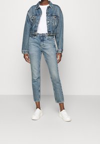 Ljust blå denimjacka med croppad längd och två framfickor, ihop med högmidjade ljusblå jeans. Bärs med vita sneakers.