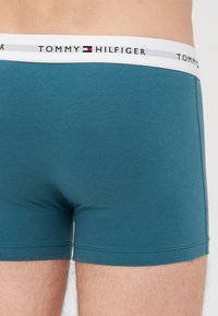 Tommy Hilfiger férfi boxer alsónadrág; türkiz színű pamut anyag, testhezálló kialakítás, fehér elasztikus derékpánt fekete, piros és kék márkalogóval.