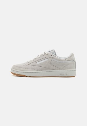 Light gray suede sneaker with white accents, textured rubber outsole, and flat laces. Features branding on the side and heel. Low-top design.