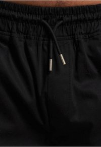 Sorte sportsshorts med elastisk talje og snøre, sølvfarvede metalspidser og en glat tekstur. Ingen synlige lommer.