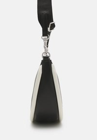 Bolso negro y crema con forma triangular, con un acabado de cuero suave, una correa texturizada y detalles en metal plateado.