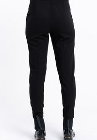 Osoba w dopasowanych czarnych spodniach, w połączeniu z czarnymi botkami za kostkę, które mają pętelkę i ribbowany szczegół przypominający skarpetę.