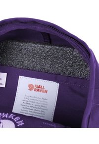 Mochila Kånken Mini da Fjällräven em púrpura, com um interior forrado em cinza suave, fecho com zíper e um rótulo com informações sobre reciclagem.