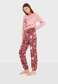 Sweatshirt rose avec un design graphique associé à un jogging rouge à motifs de fleurs et de papillons, avec des poignets fuselés et une taille à cordon.