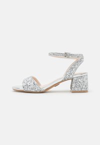 Sandali con tacco glitterati argento, con cinturino alla caviglia, punta aperta e tacco a blocco. Presentano un elegante dettaglio metallico e una superficie glitterata testurizzata.