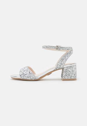 Glittery silver heeled sandals with an ankle strap, open toe, and block heel. Features a smooth metallic accent and textured glitter surface.