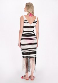 Virkat klänning med svart och vitt randigt mönster, V-ryggdesign och fransar vid kanten. Utsmyckad med ett rosa band vid halsen.