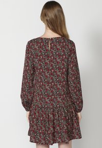 Schwarzes Kleid mit rotem Blumenmuster, langen Ärmeln, gerafftem Saum und einem Schlüsselloch-Rückendetail. Aus leichtem Stoff gefertigt.