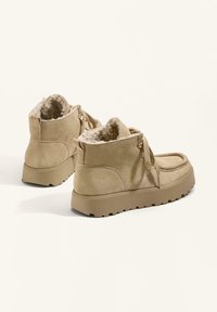 Béžové semišové členkové čižmy s jemným, nadýchaným podšíváním, okrúhlou špičkou a štruktúrovanou gumovou podrážkou. Obsahujú prednú šnúrku a prešitie.